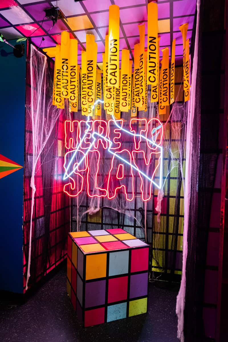 A neon "HERE TO SLAY" sign above a Rubik's cube table