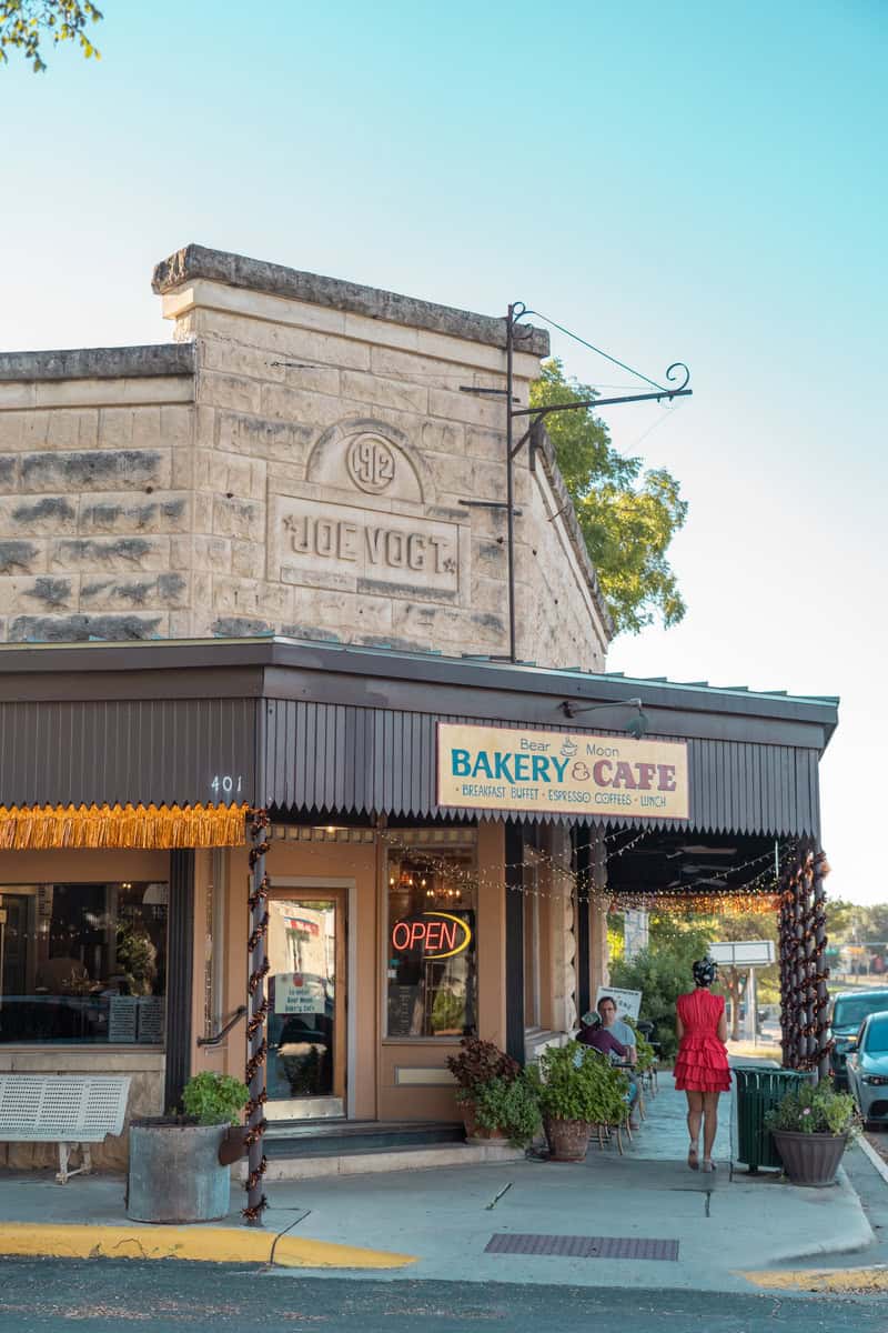 Person walking past a bakery and cafe with "OPEN" sign