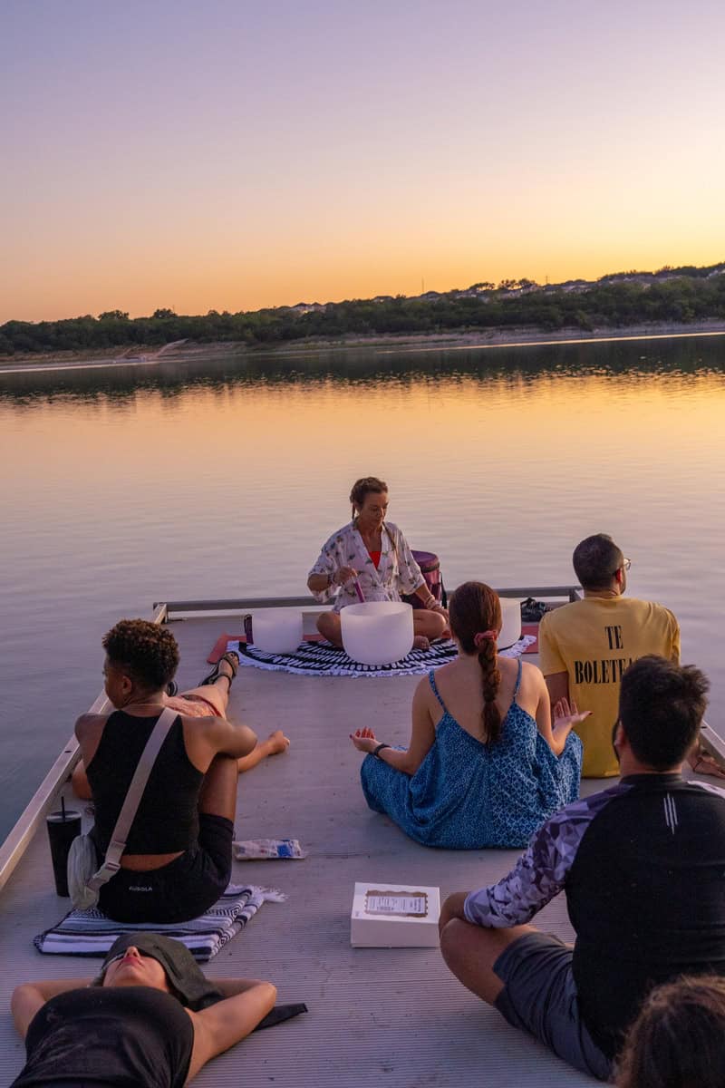 Group of people in a meditation session on a dock at sunset.