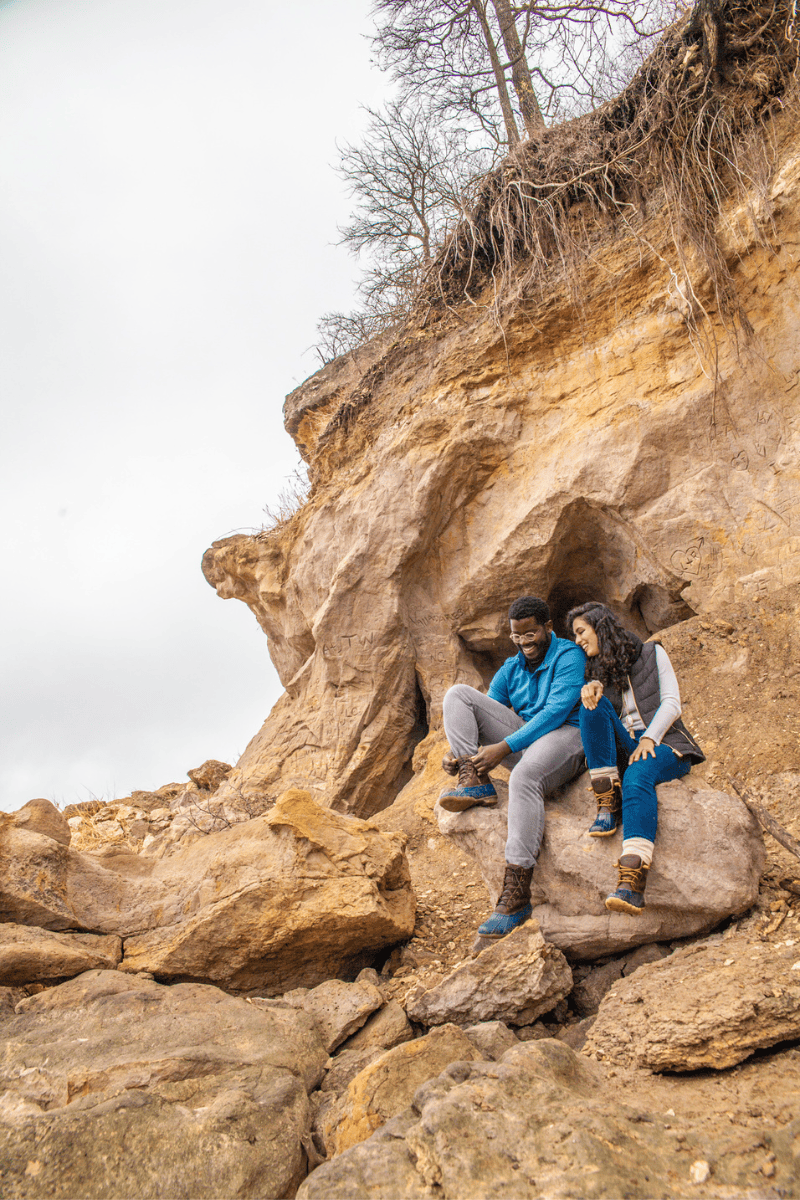 Two individuals sitting together on a rocky outcrop under a bare tree.