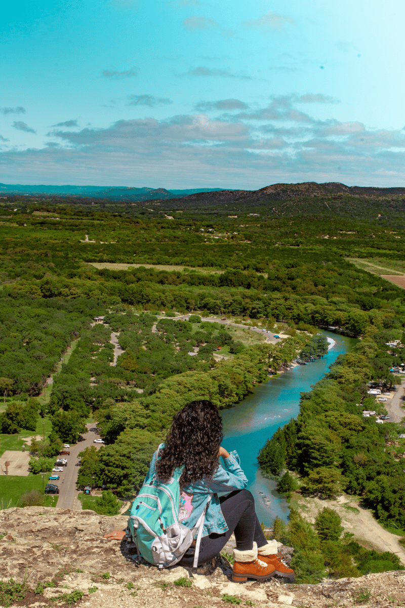 Person sitting on a cliff overlooking a winding river and green landscape.