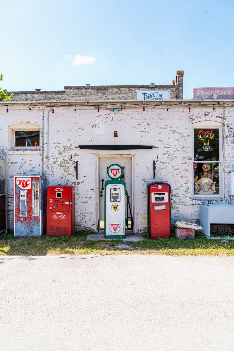 Rustic building with vintage gas pumps and soda machines outside.