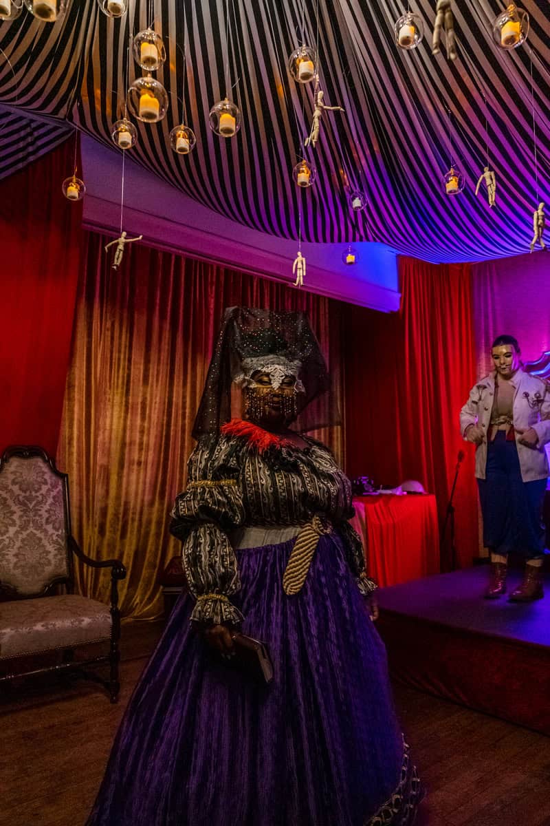 A woman wearing a vibrant costume poses in front of a stage,