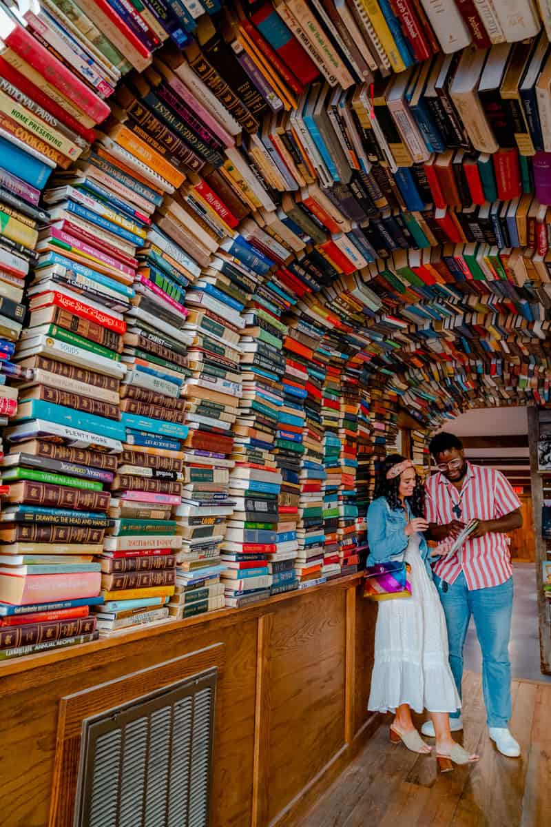 Two people standing by a towering arch of colorful stacked books.