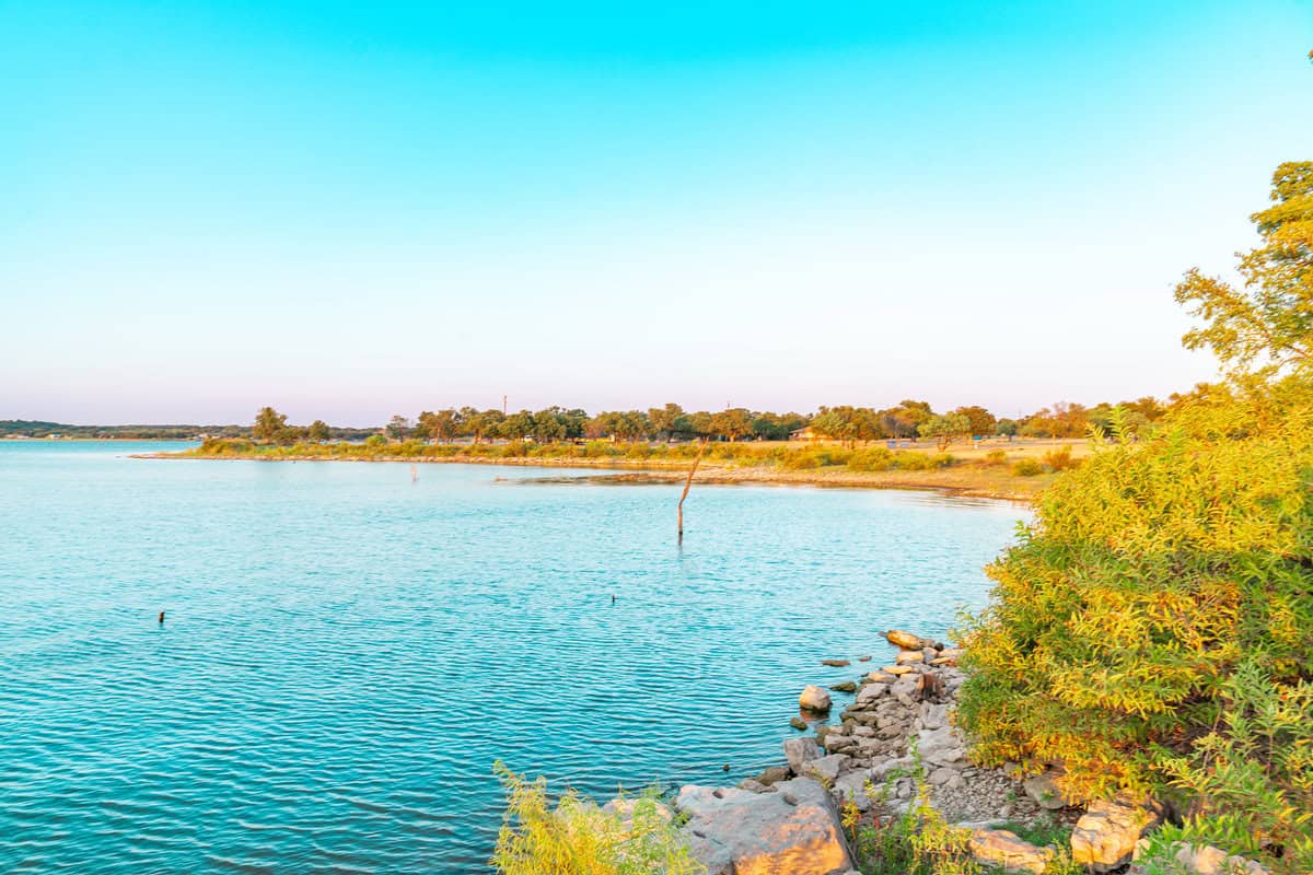 Tranquil lake with rocky shore and trees at sunset.