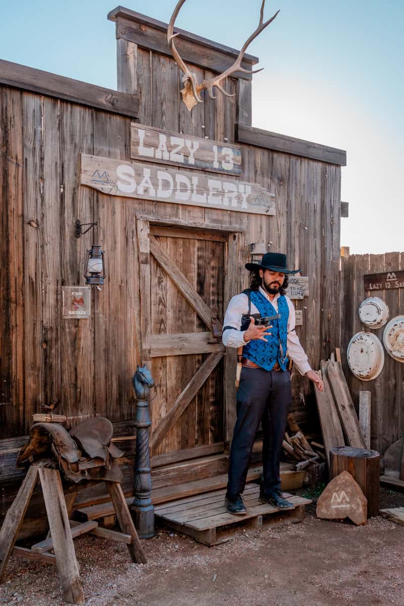 Person in cowboy attire stands by a wooden building