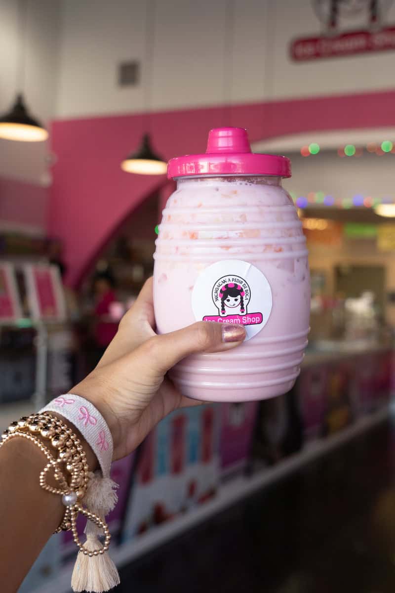 A person's hand holding a pink milkshake jar in an ice cream shop.