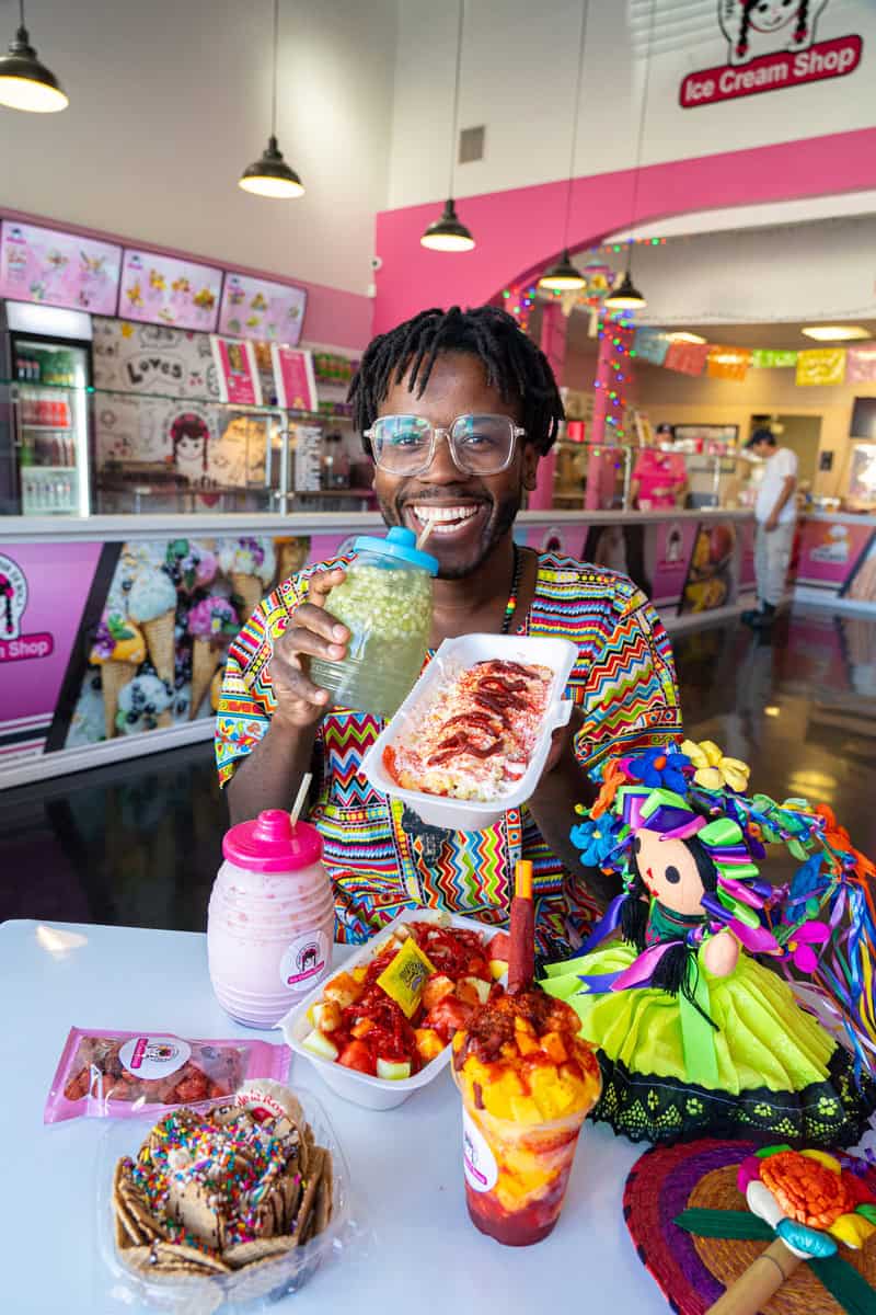 Person holding food with colorful treats on a table in an ice cream shop.