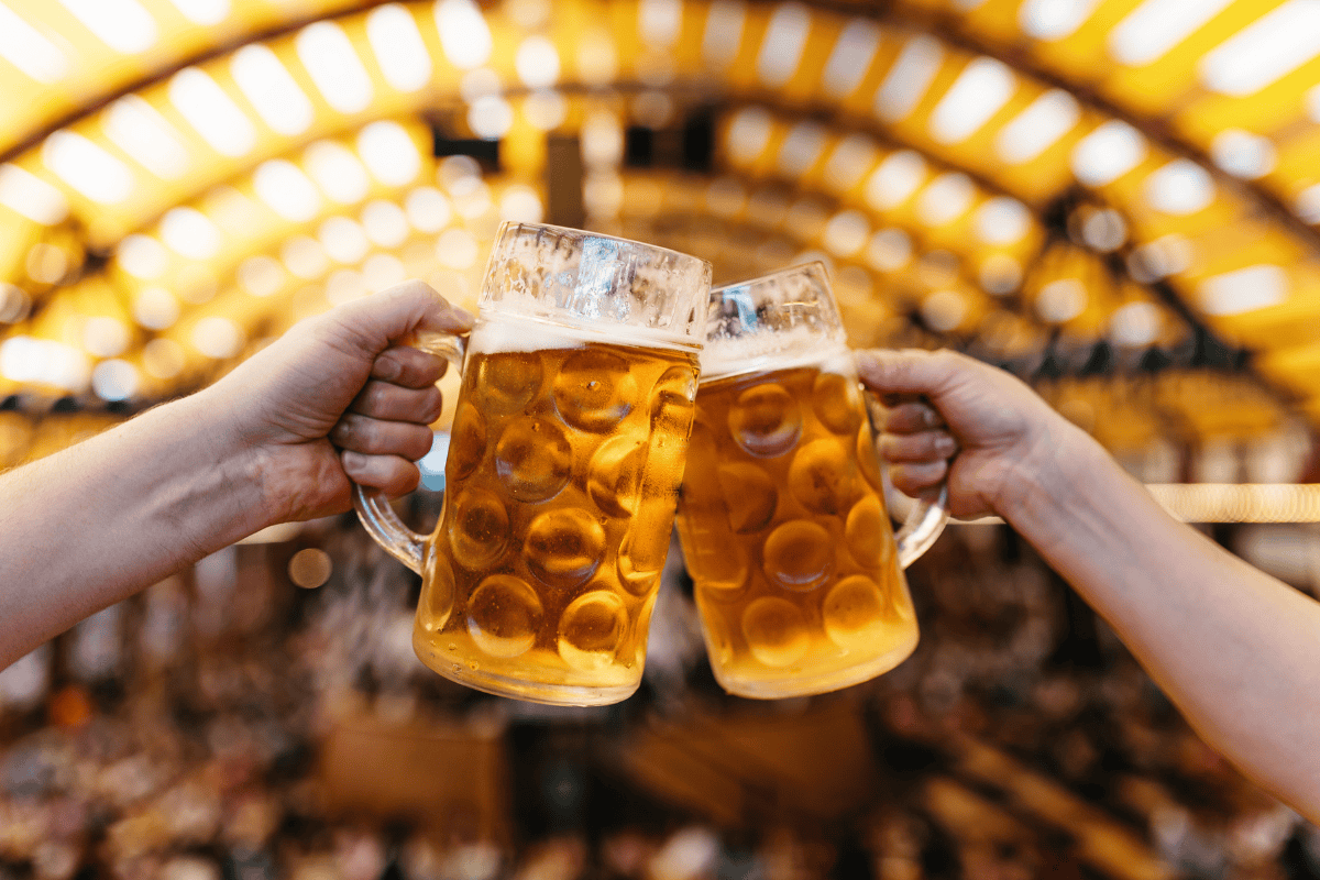 Two individuals raise their beer mugs in a toast at a lively beer festival