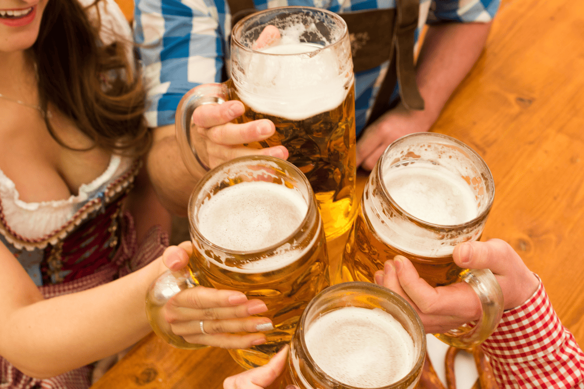 People toasting with large beer mugs on a wooden table.