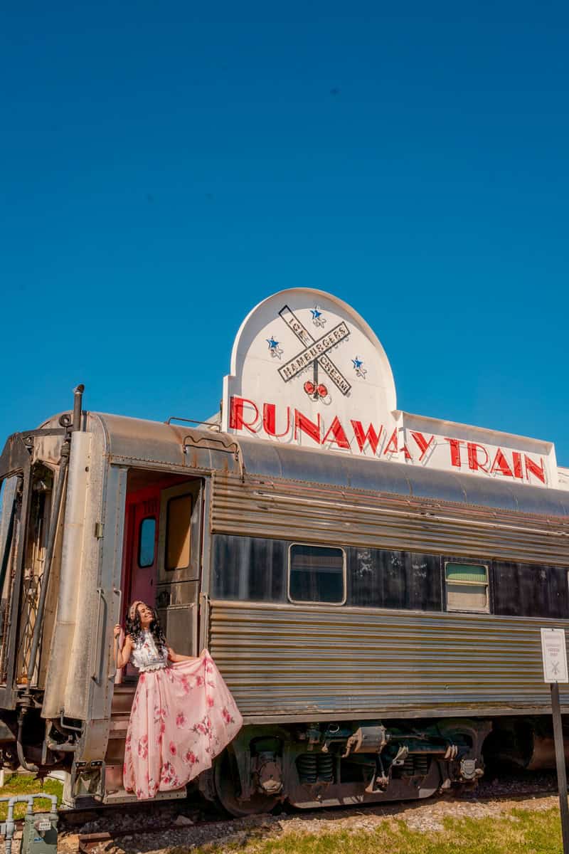 A woman in a dress sits gracefully on the side of a train