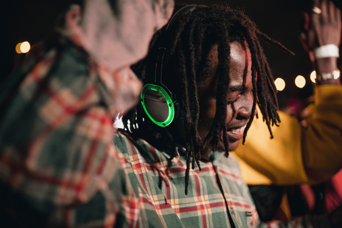 Person in plaid shirt with green-lit headphones around neck at night.