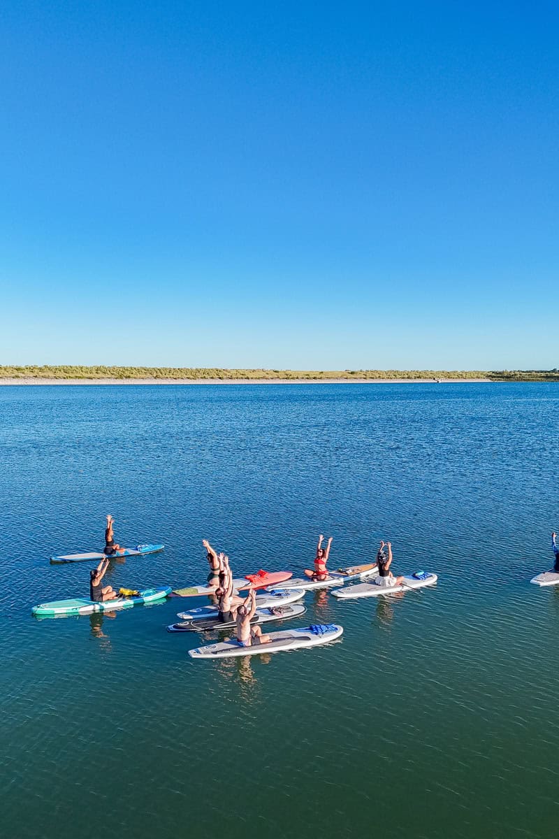 People practicing yoga on paddleboards on a calm blue lake.