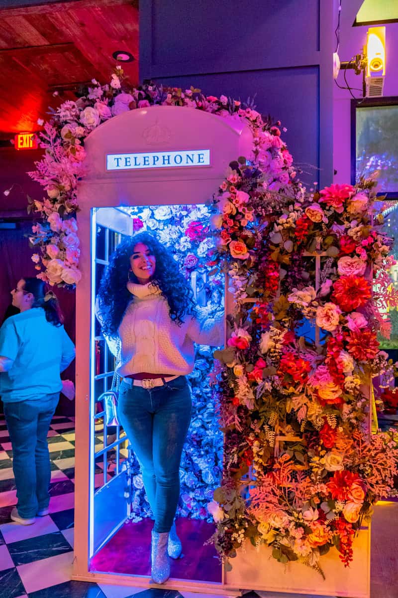 A person stands in a vibrantly flower-adorned telephone booth