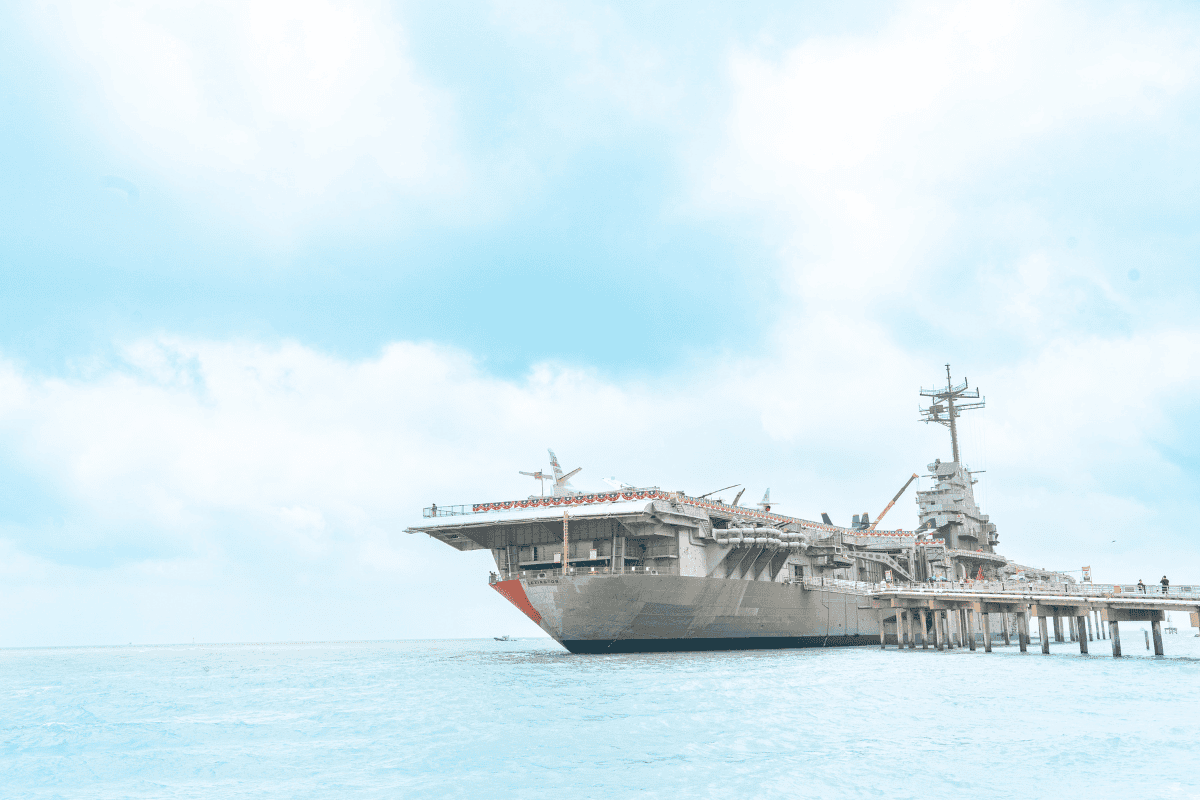 Aircraft carrier docked on a clear day with open sky and calm sea.