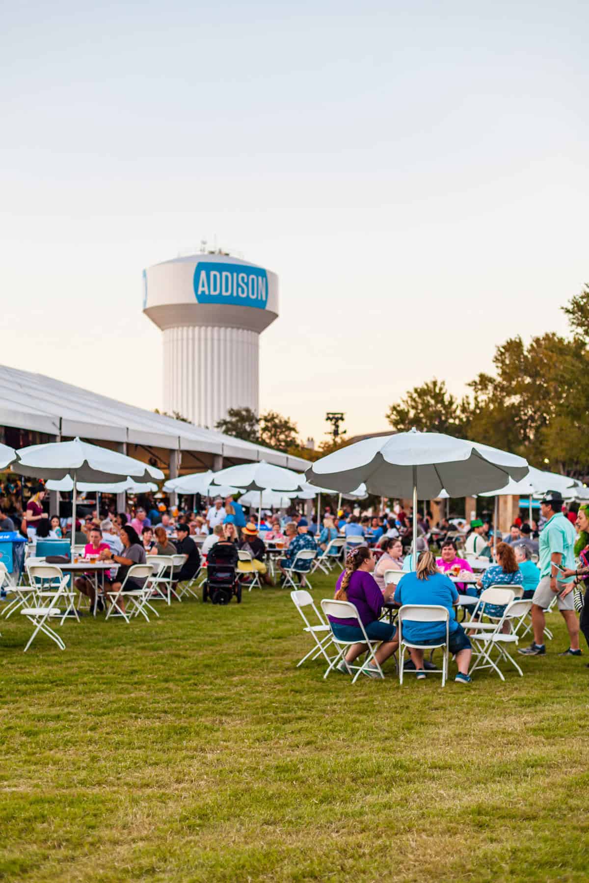 Outdoor event with people sitting at tables under umbrellas