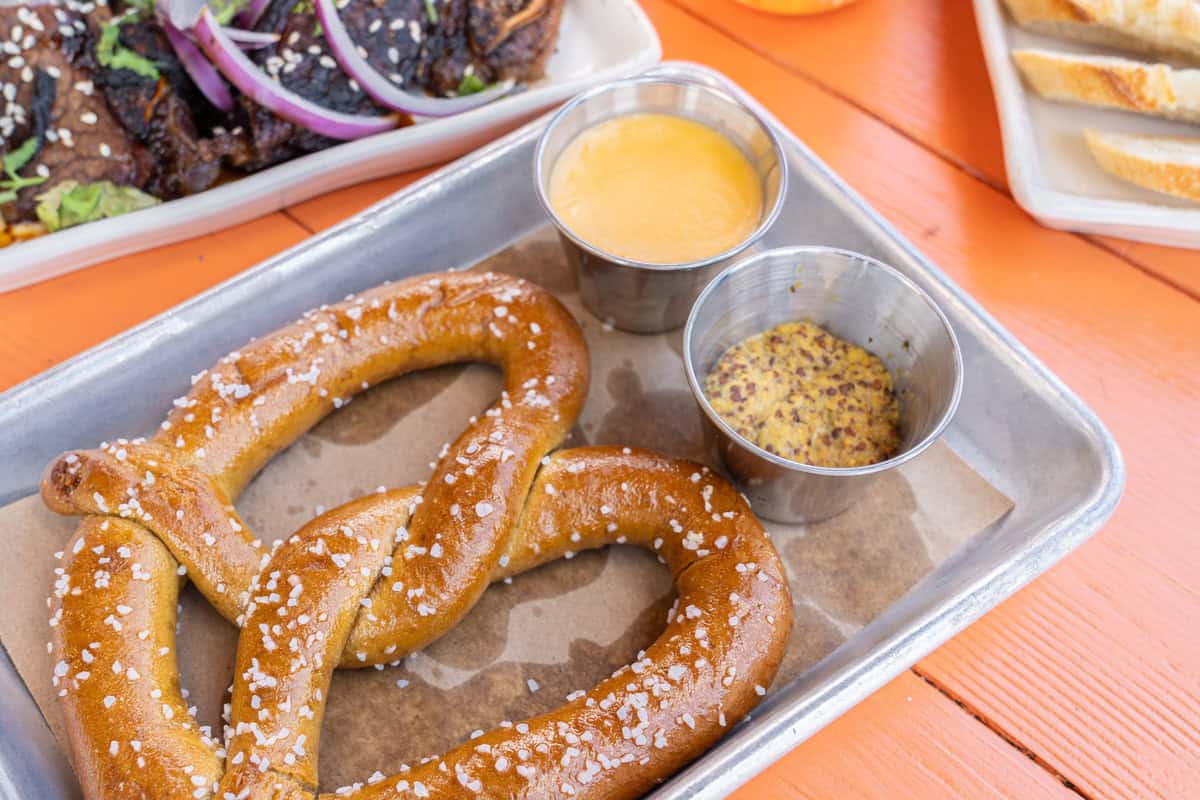 Salted soft pretzels with mustard and cheese dip on a metal tray.