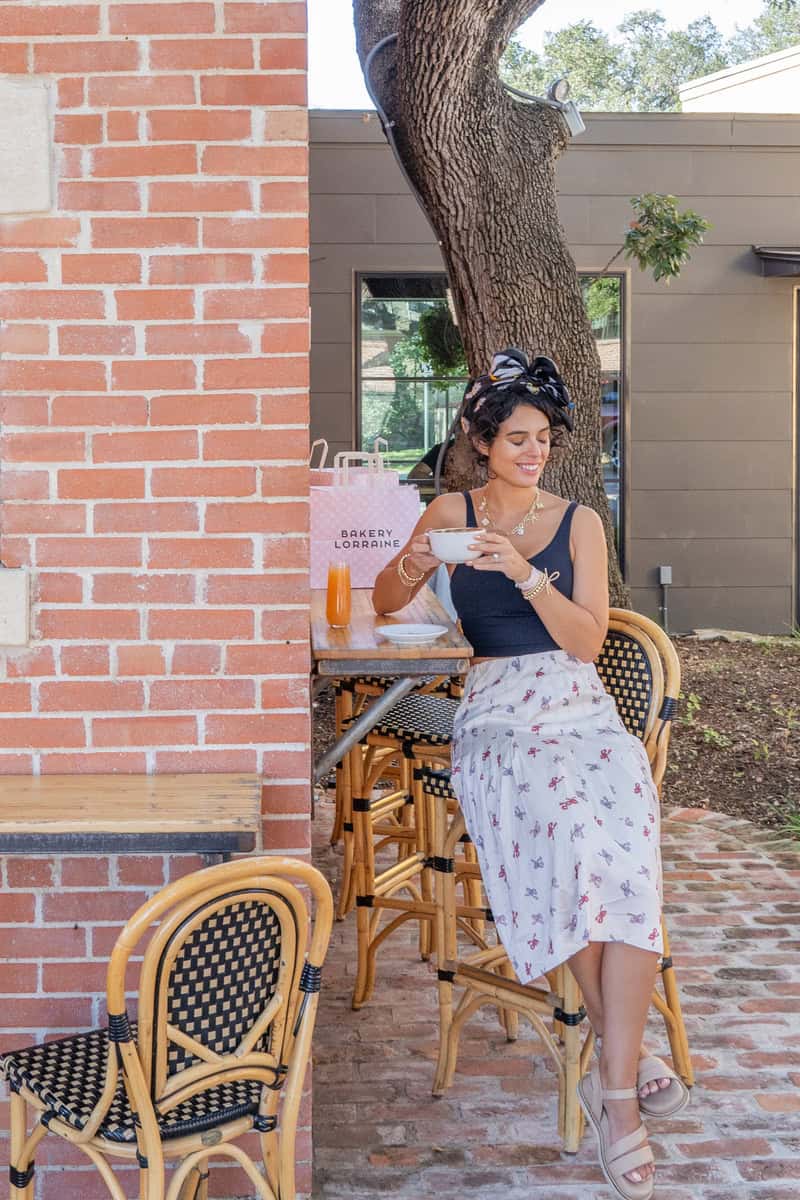 Person sitting at an outdoor cafe with a bowl in hand and a shopping bag on the table.