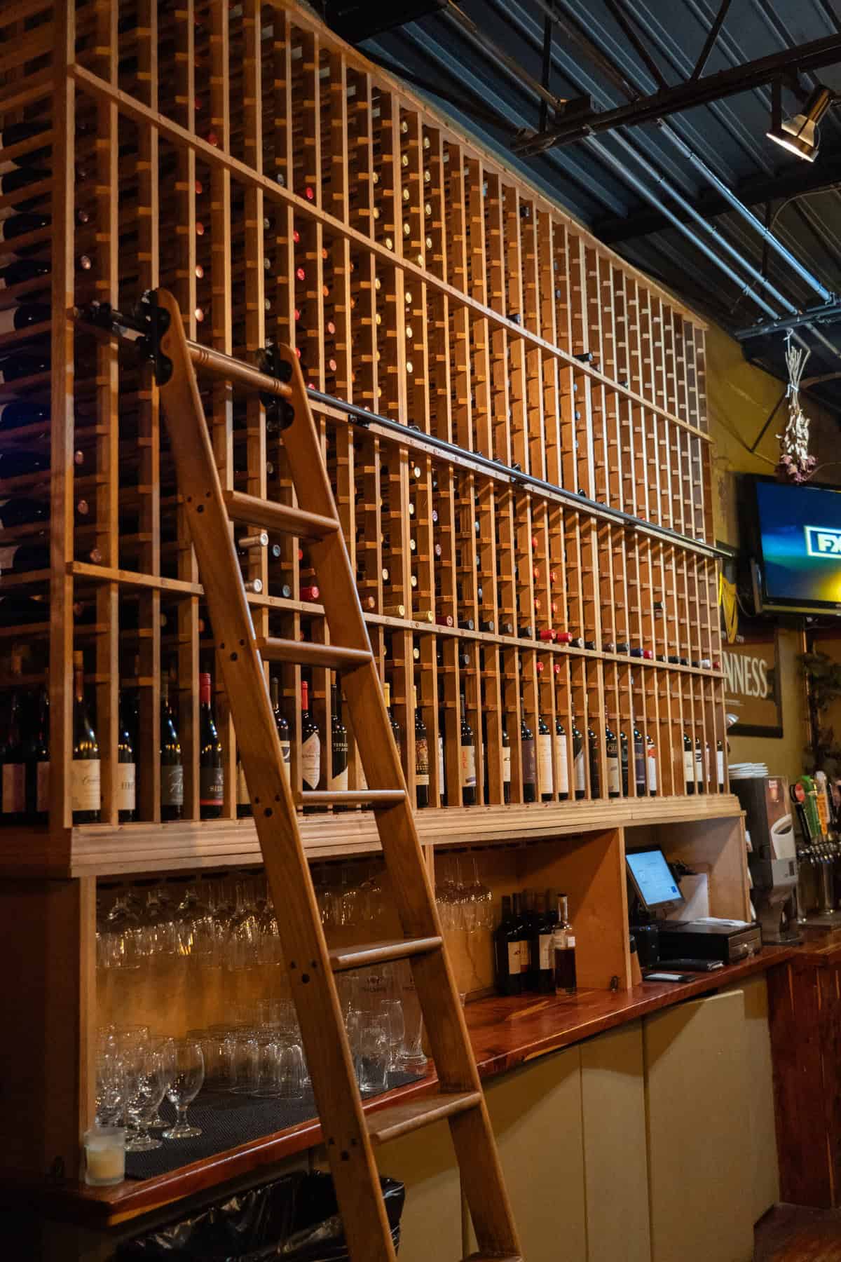 A tall wine rack accessed by a wooden ladder in a bar