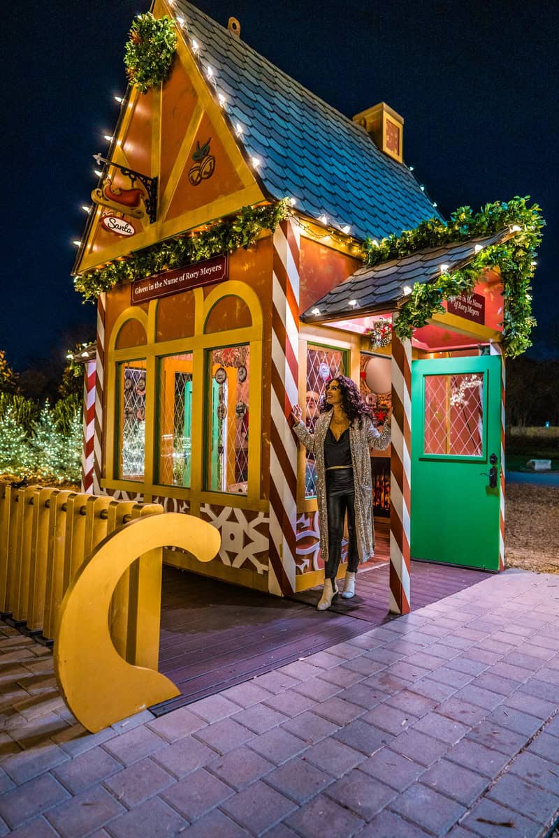 Person standing by a festive, candy cane-striped holiday hut adorned