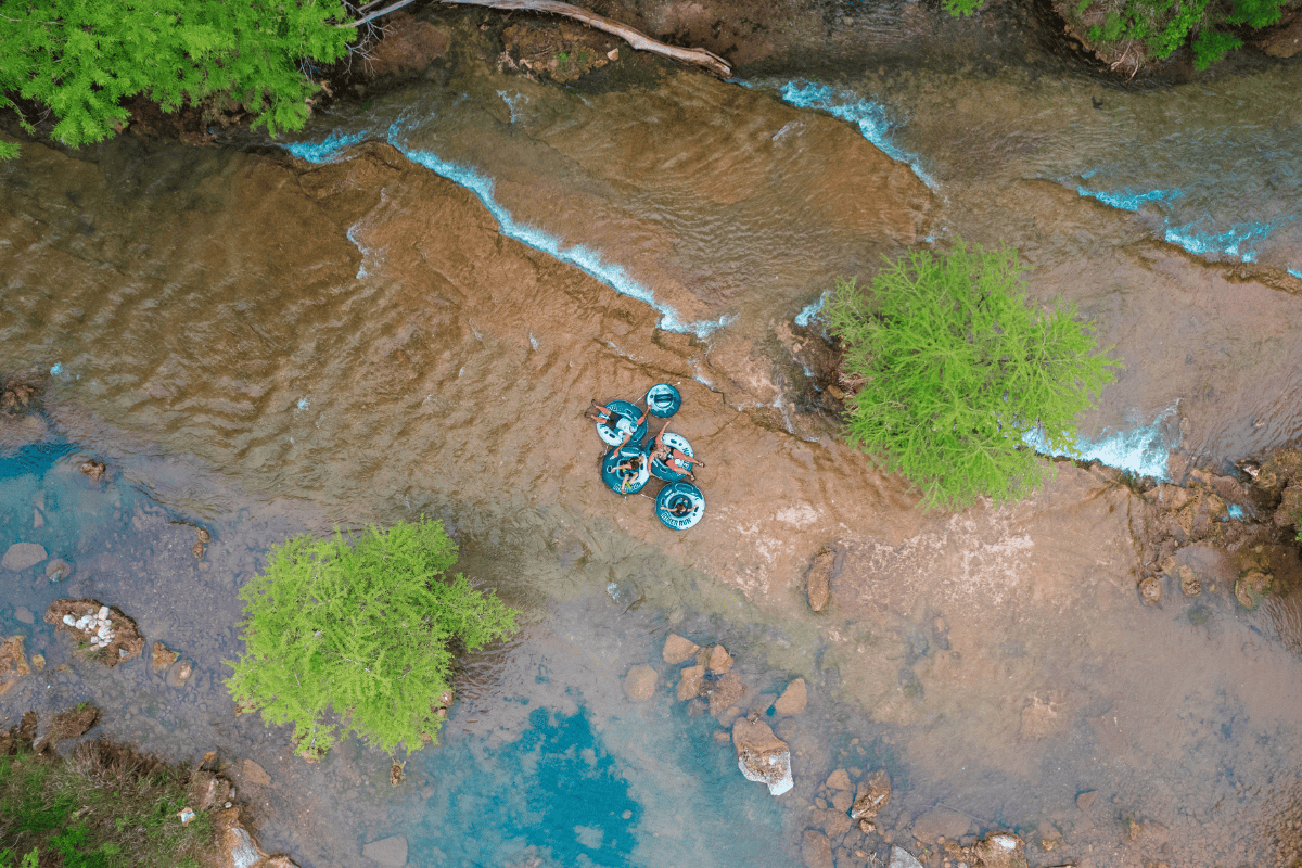 Aerial view of three people on colorful tubes in a shallow river