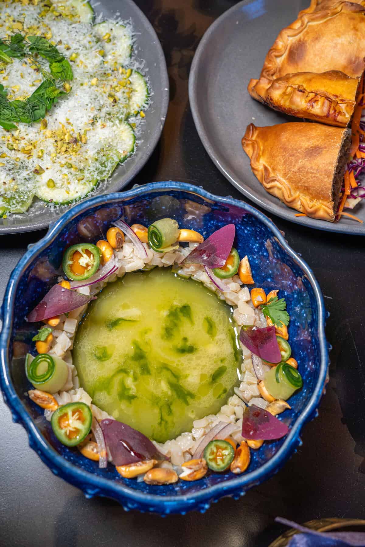 A colorful bowl of soup with toppings and empanadas on a table.