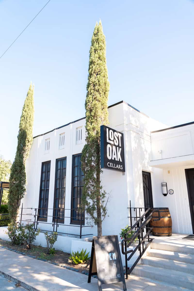 White building with "Lost Oak Cellars" sign and tall cypress trees