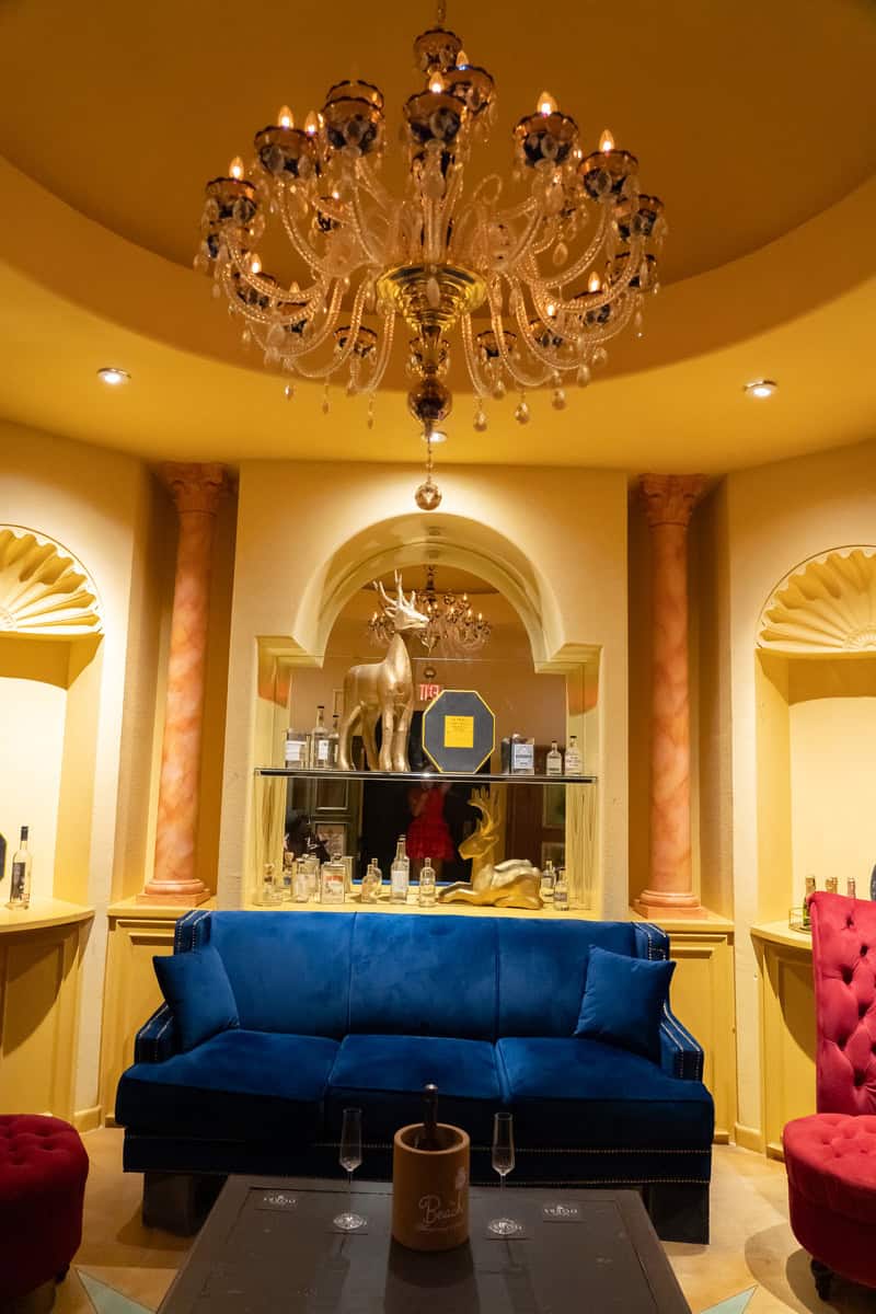 Opulent room with blue velvet sofa, large chandelier, and mirrored bar