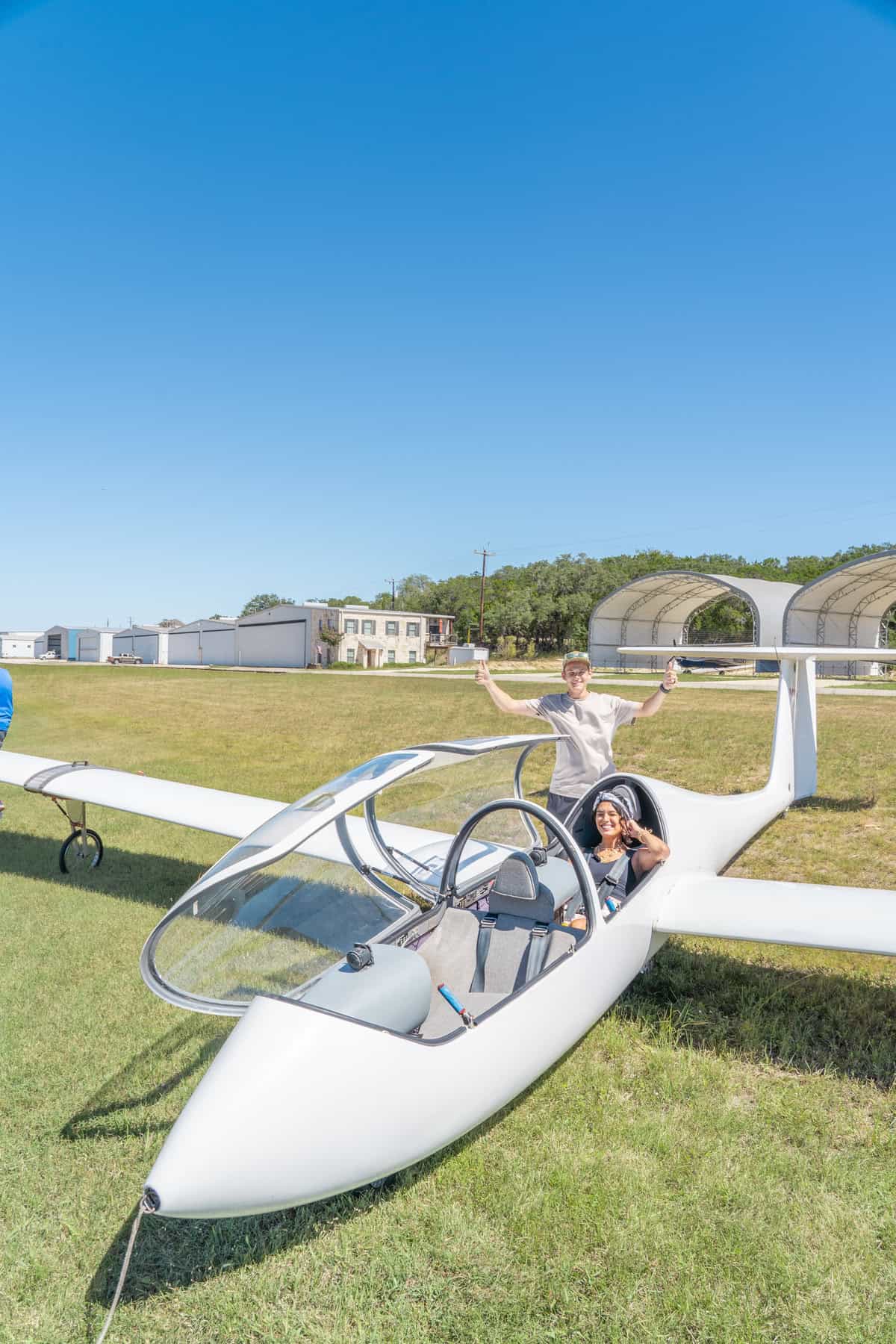 Person in a white glider on a grassy field, with clear blue skies above.