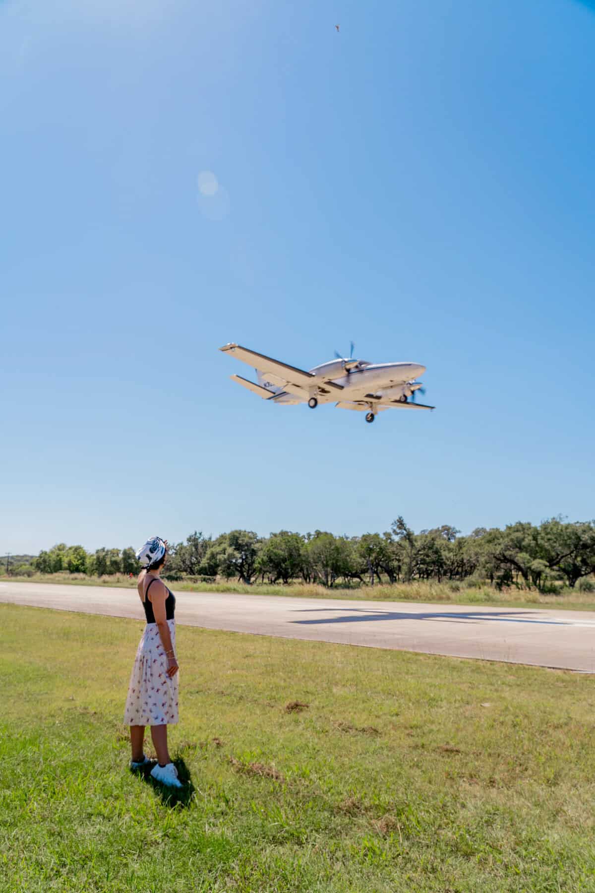 A person watching a low-flying plane near an airstrip on a clear day.