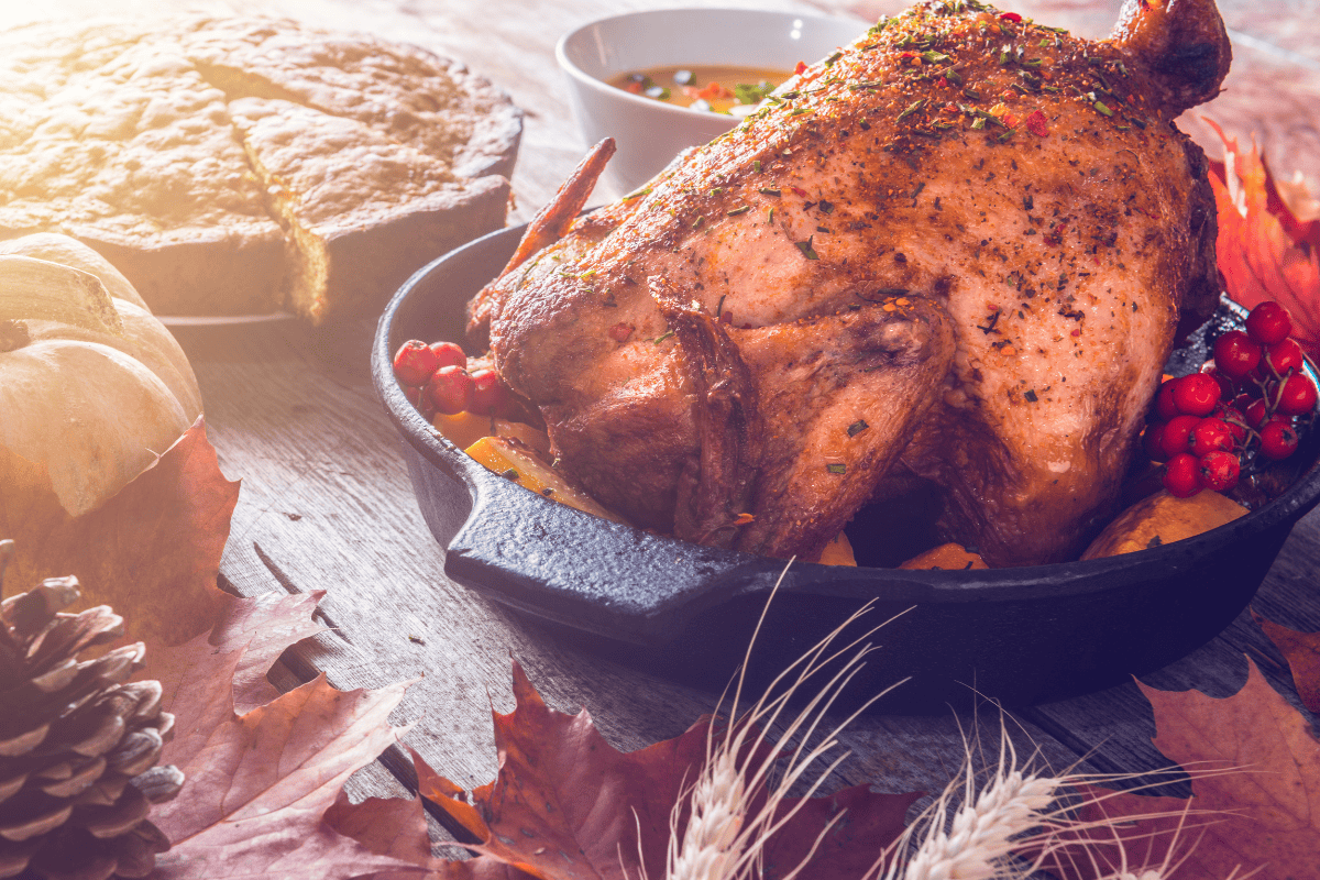 Roasted chicken in a skillet, with pie and autumn decorations on a table.