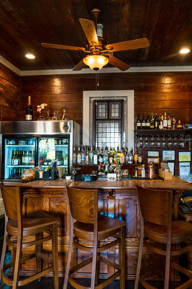 Cozy bar interior with wooden walls, bar stools, and a ceiling fan.