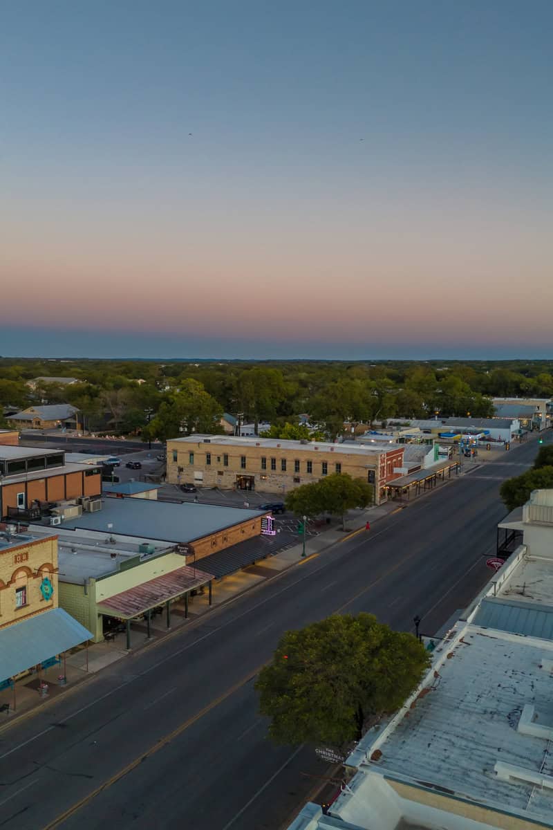 Aerial view of a small town at dusk with pastel sky and lit streetlights.