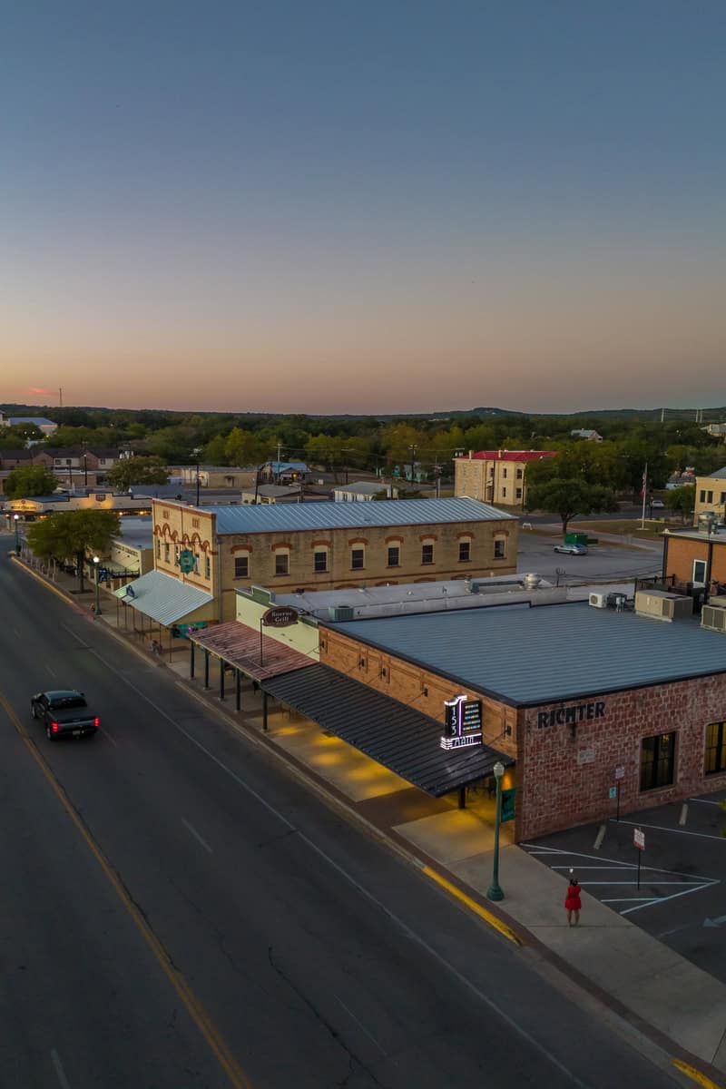 Twilight view of a street with historic buildings, a single car, and a pedestrian.