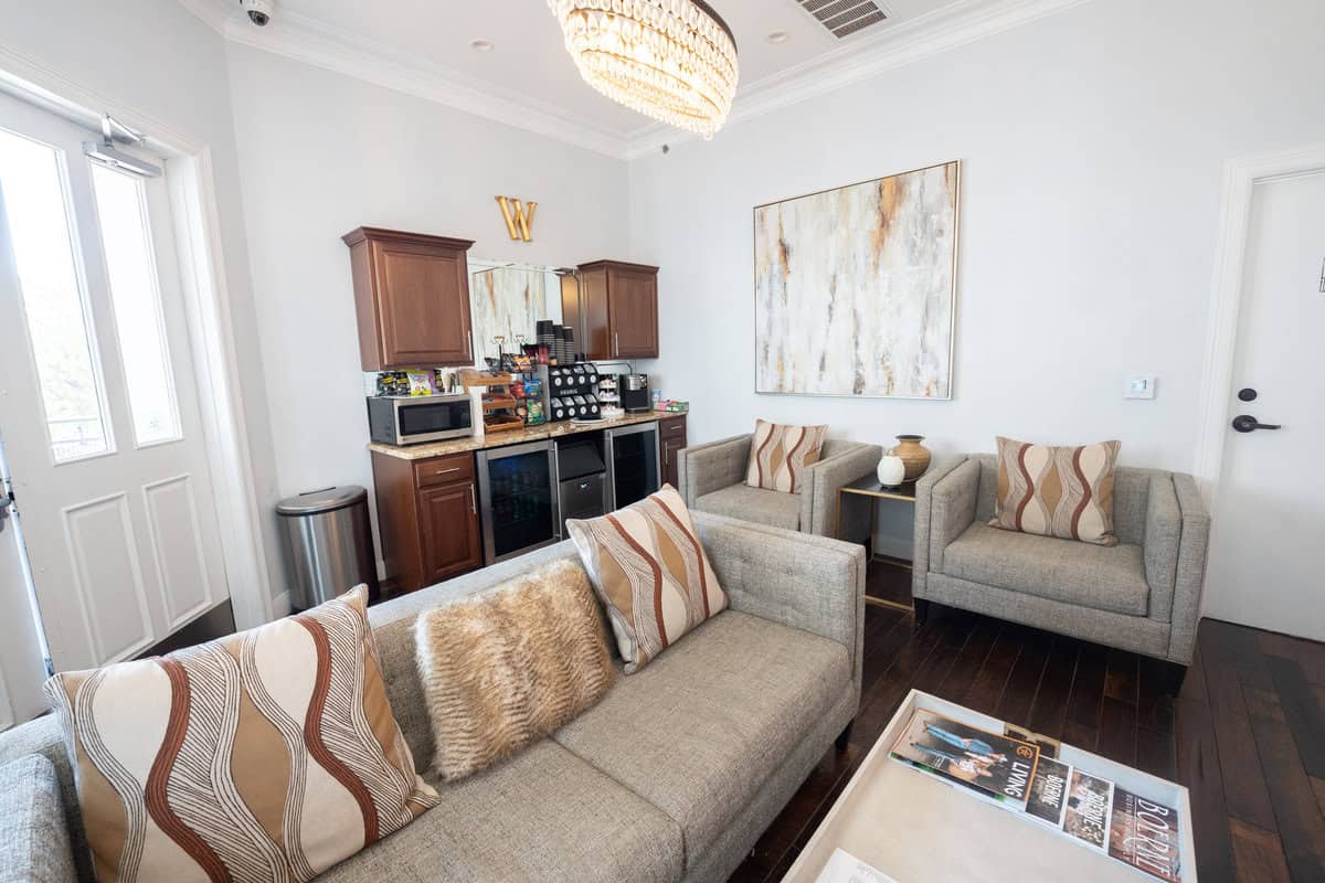 Elegant living room with kitchenette, beige sofa, two armchairs, and abstract art.