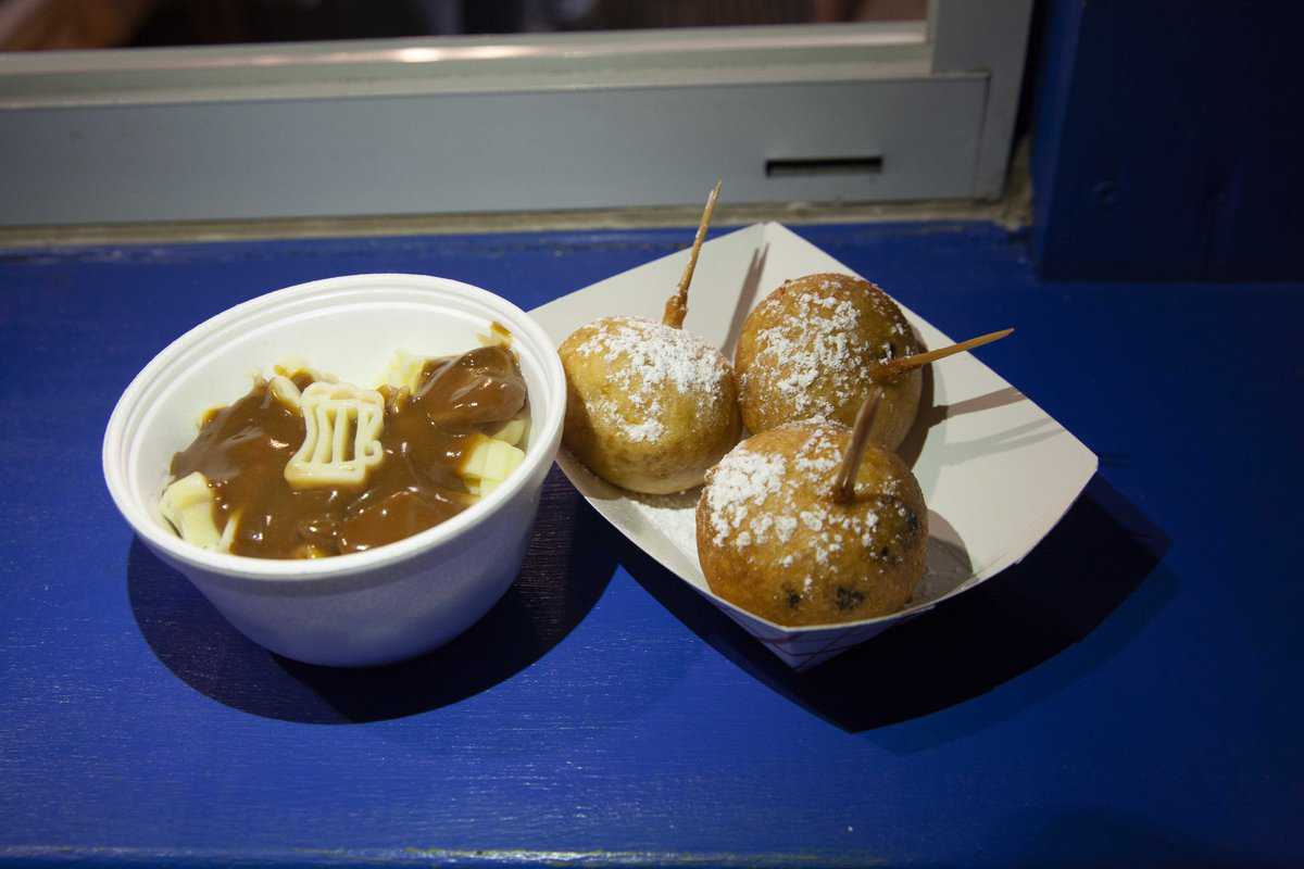 Bowl of poutine and three deep-fried snacks on skewers on a blue counter.