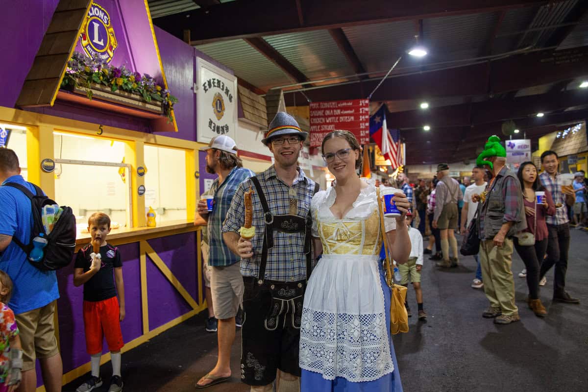 People at a fair with traditional German outfits holding drinks.