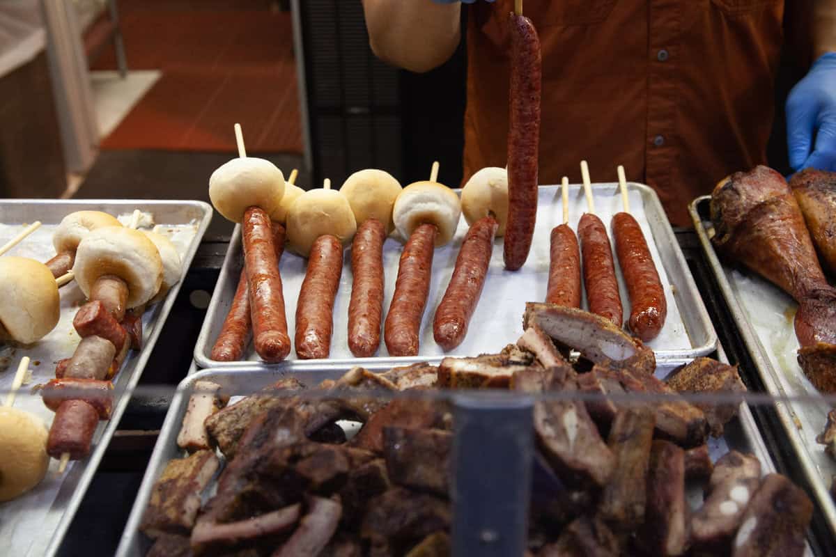 A street food vendor displays various grilled sausages and meats