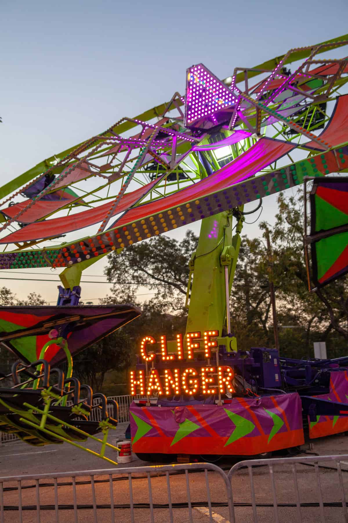 Amusement park ride "Cliff Hanger" with neon lights at dusk.