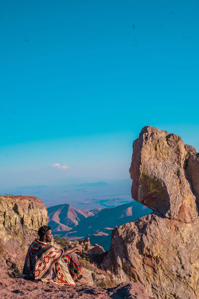 Person in colorful clothing sitting on a mountain overlooking a valley.