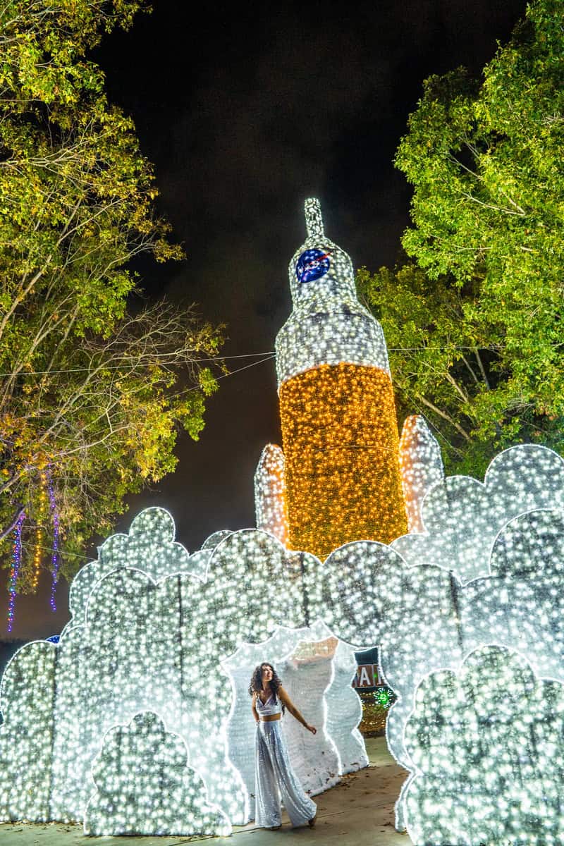 Woman posing in front of illuminated bottle-shaped light display at night