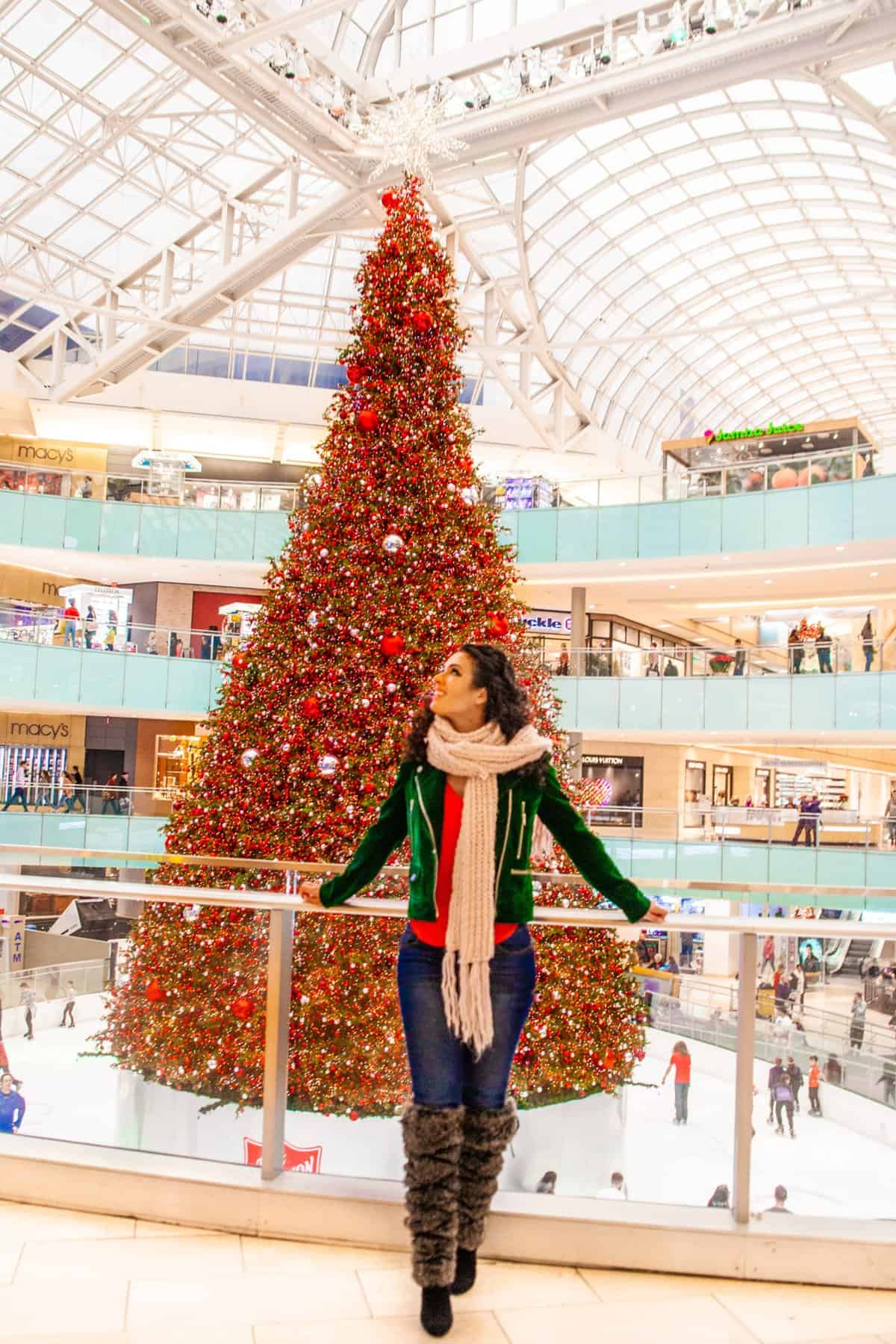 A woman smiles while standing in front of a beautifully decorated Christmas tree.