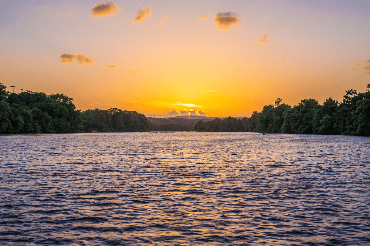 Sunset over a rippled lake with trees on the horizon and a colorful sky.