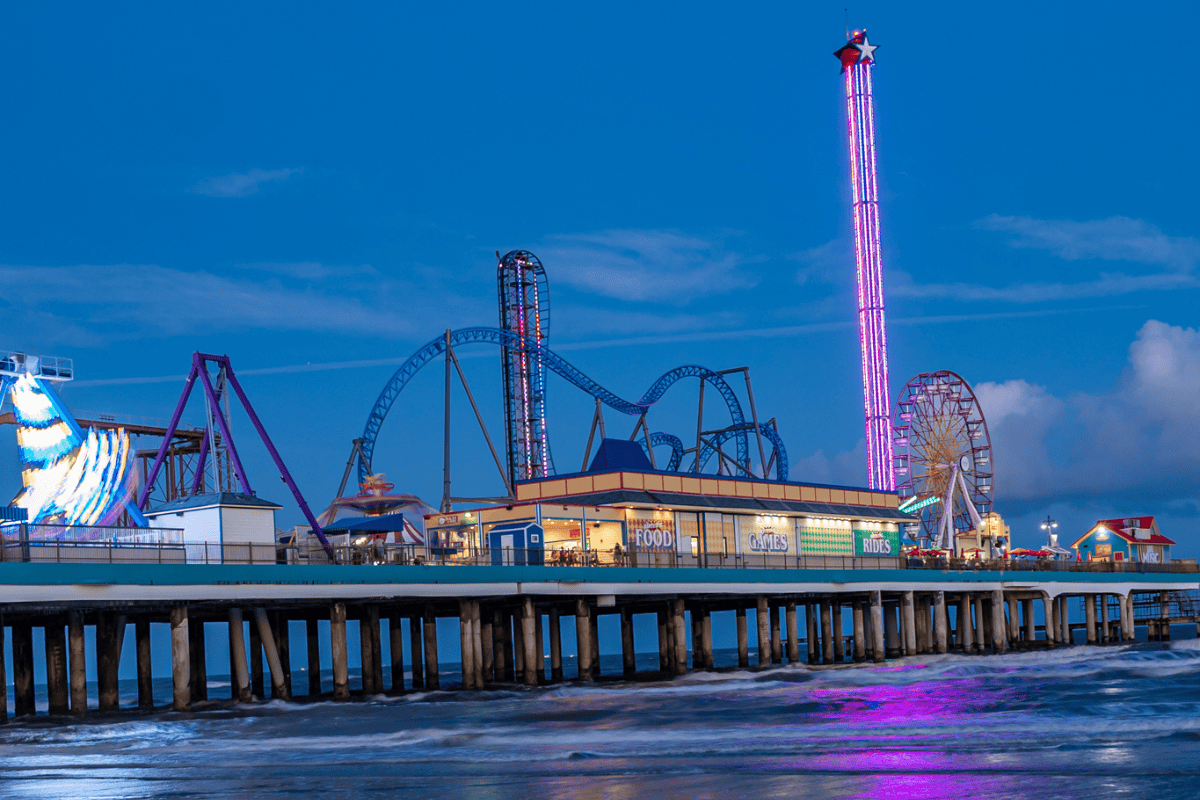 Illuminated amusement park pier with roller coaster and Ferris wheel