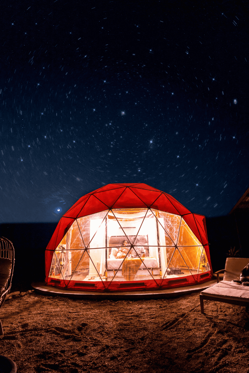 Illuminated geodesic dome under a starry night sky on the beach.