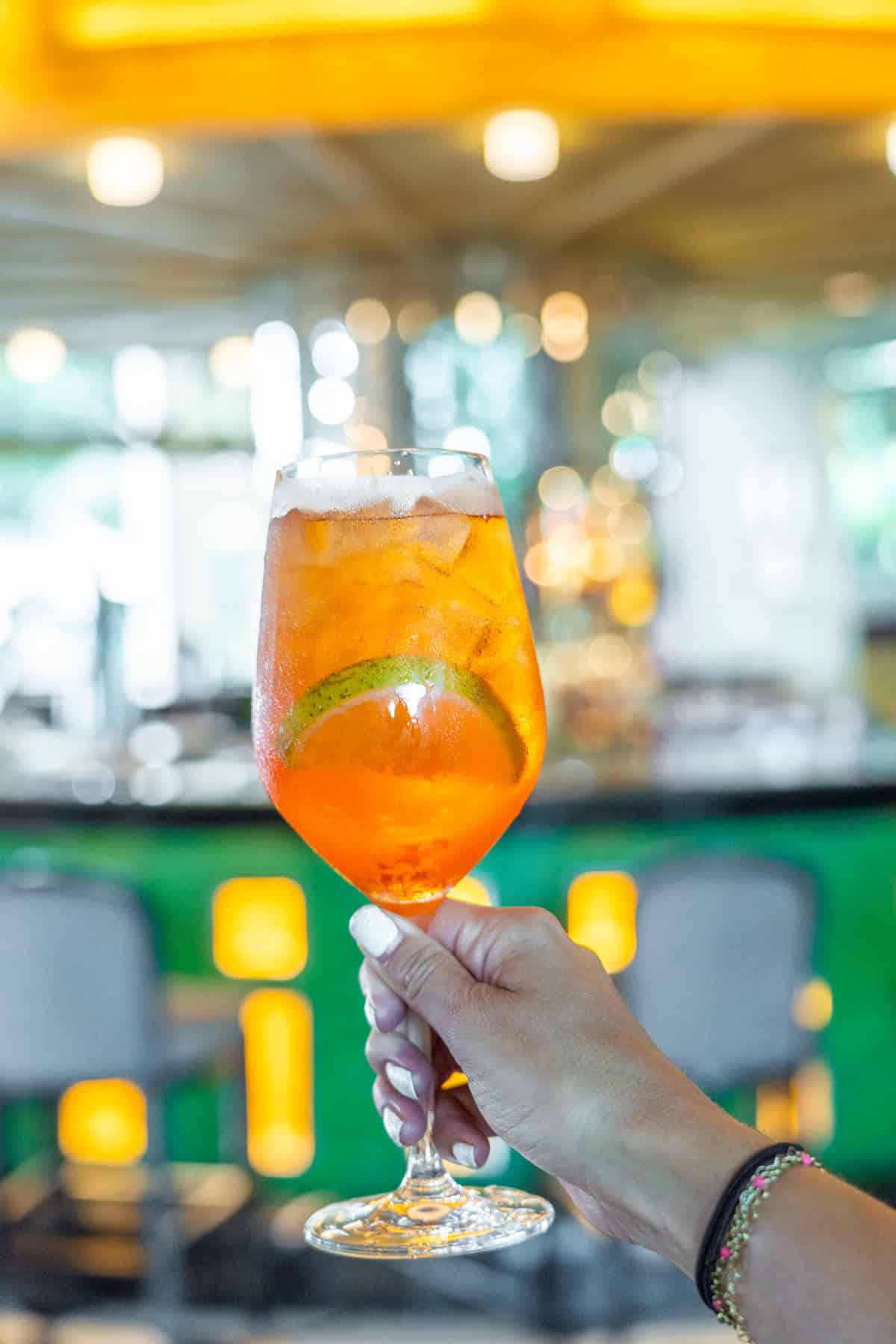 A hand holds a sparkling orange drink with ice and a lime