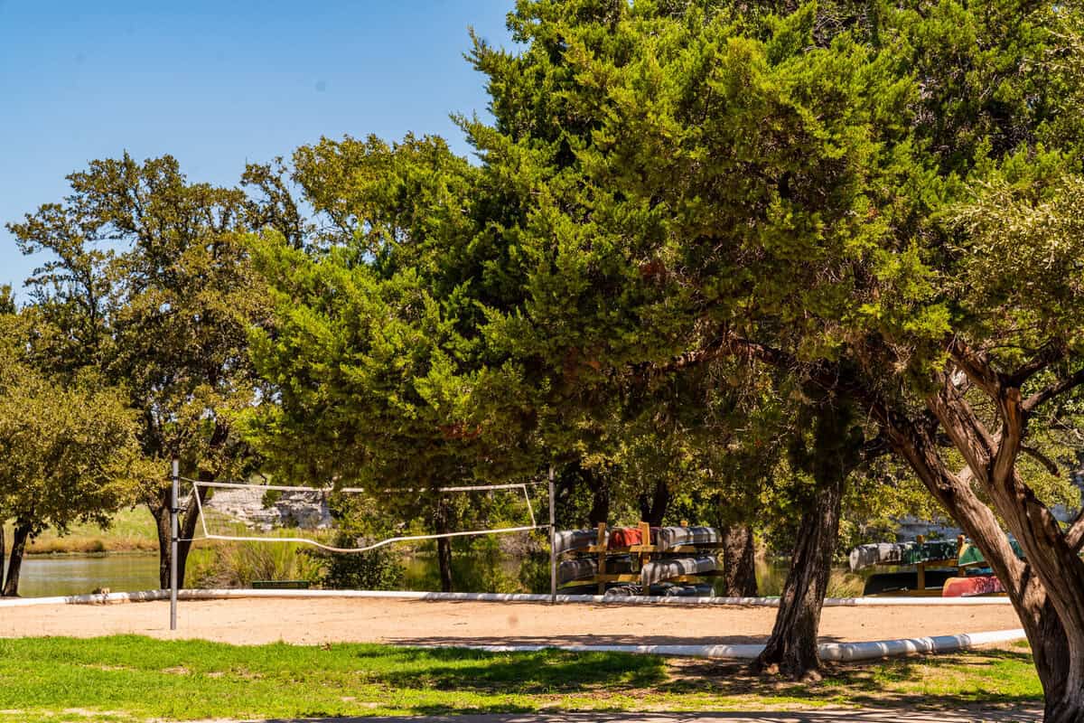 Sunny park with volleyball net, trees, and a glimpse of water.