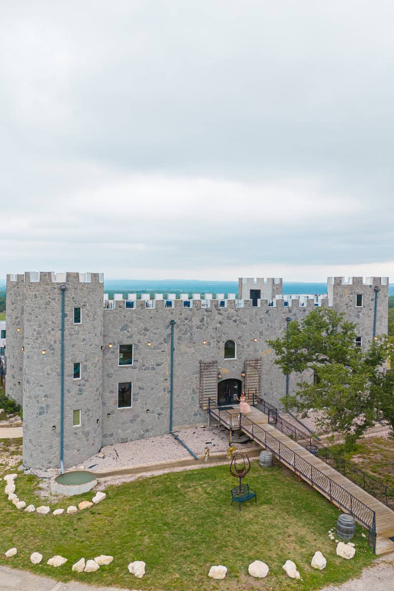 A gray stone castle with a drawbridge, surrounded by greenery and pathways