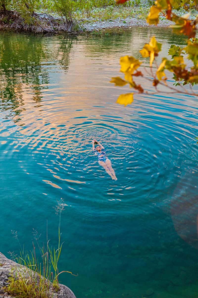 A woman swims leisurely in a serene, turquoise lake