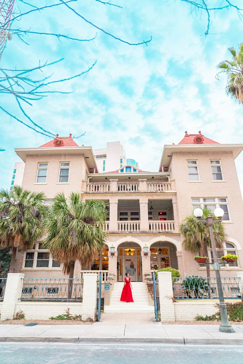 A woman in a red dress stands at the entrance of a historic building